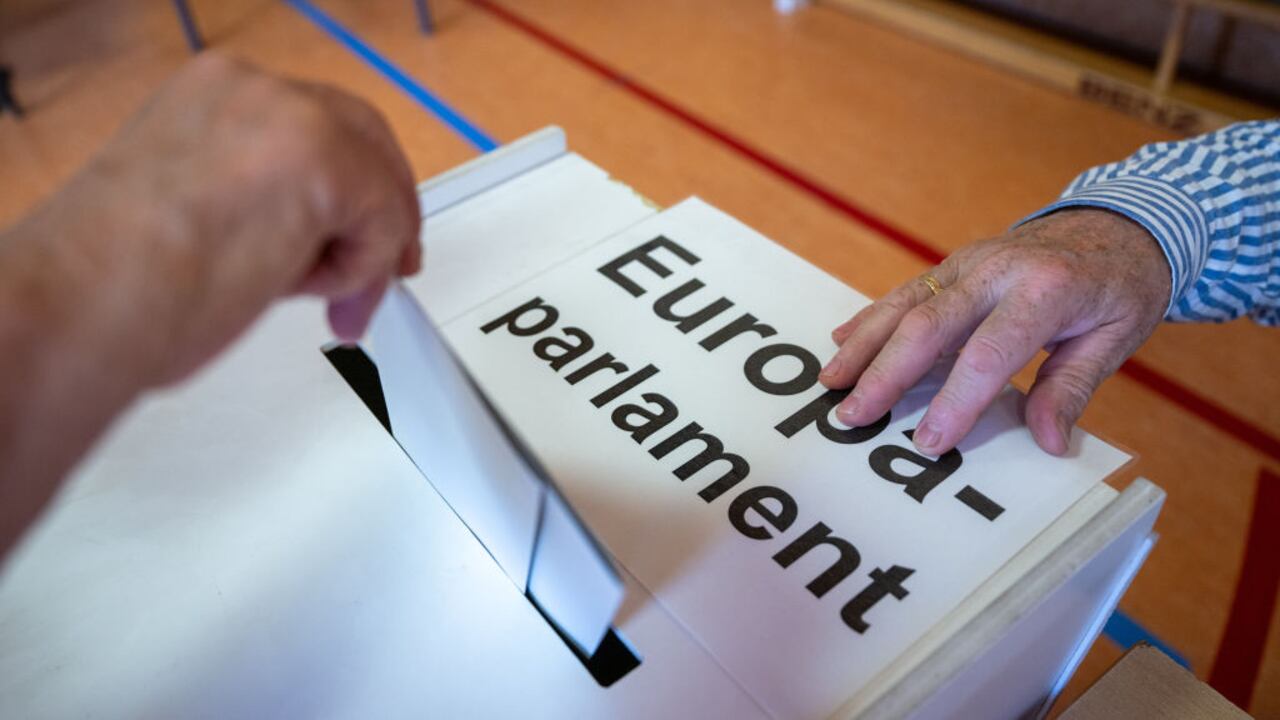Un votante deposita su voto en una urna con la etiqueta "Parlamento Europeo" en una mesa electoral.