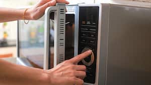 Manos de mujer cerrando la puerta del horno de microondas y preparando comida en el microondas.