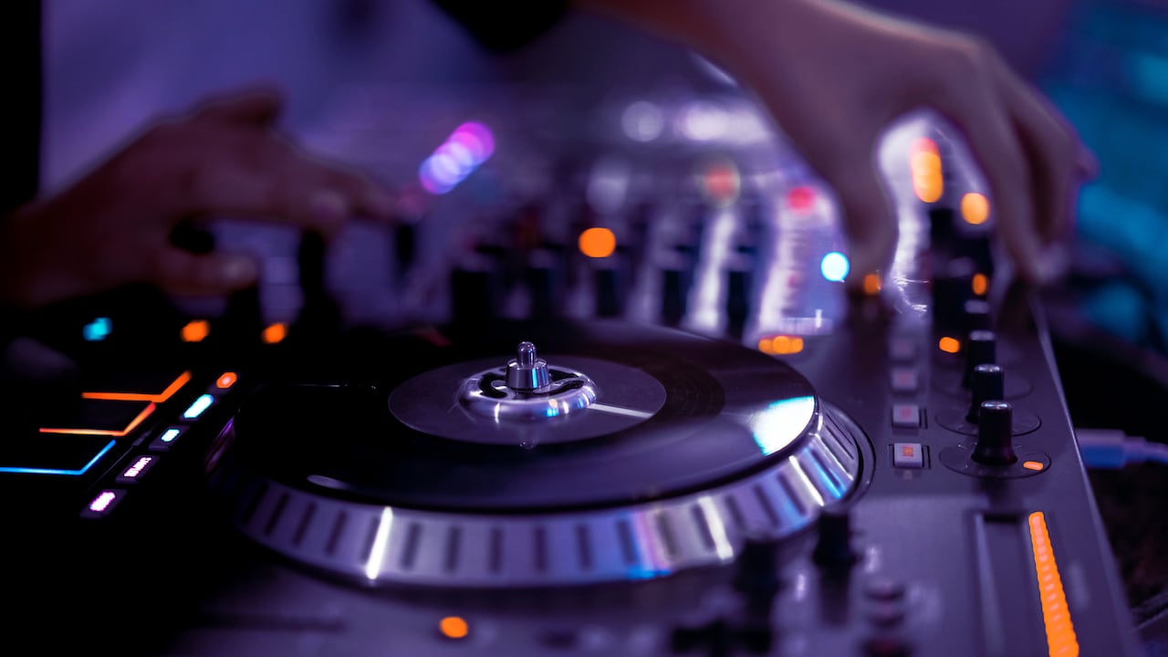 Close-up of an American DJ, working with sound, adjusting basses and high tones, spinning turntable records at a night club party in purple and very peri neon lights. Musical apps and podcasts concept