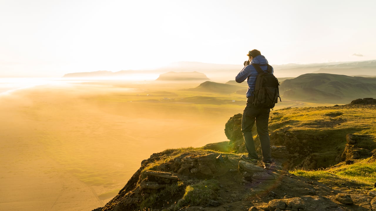 Un hombre tomando fotos de la puesta de sol desde lo alto de un acantilado en Islandia.
