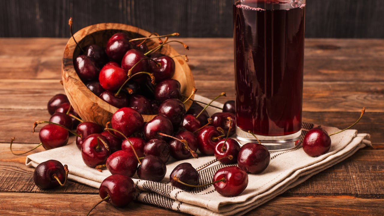 Cold cherry juice in a glass with ripe berries in bowl basket on a wooden table