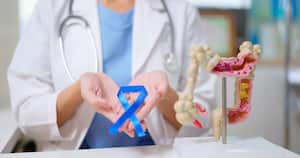 close up of female doctor hand wear white coat holds blue ribbon in front of her chest with colon model on table