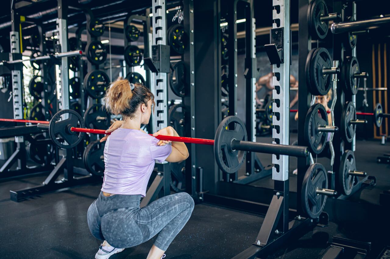 Young woman doing squats with barbell in gym