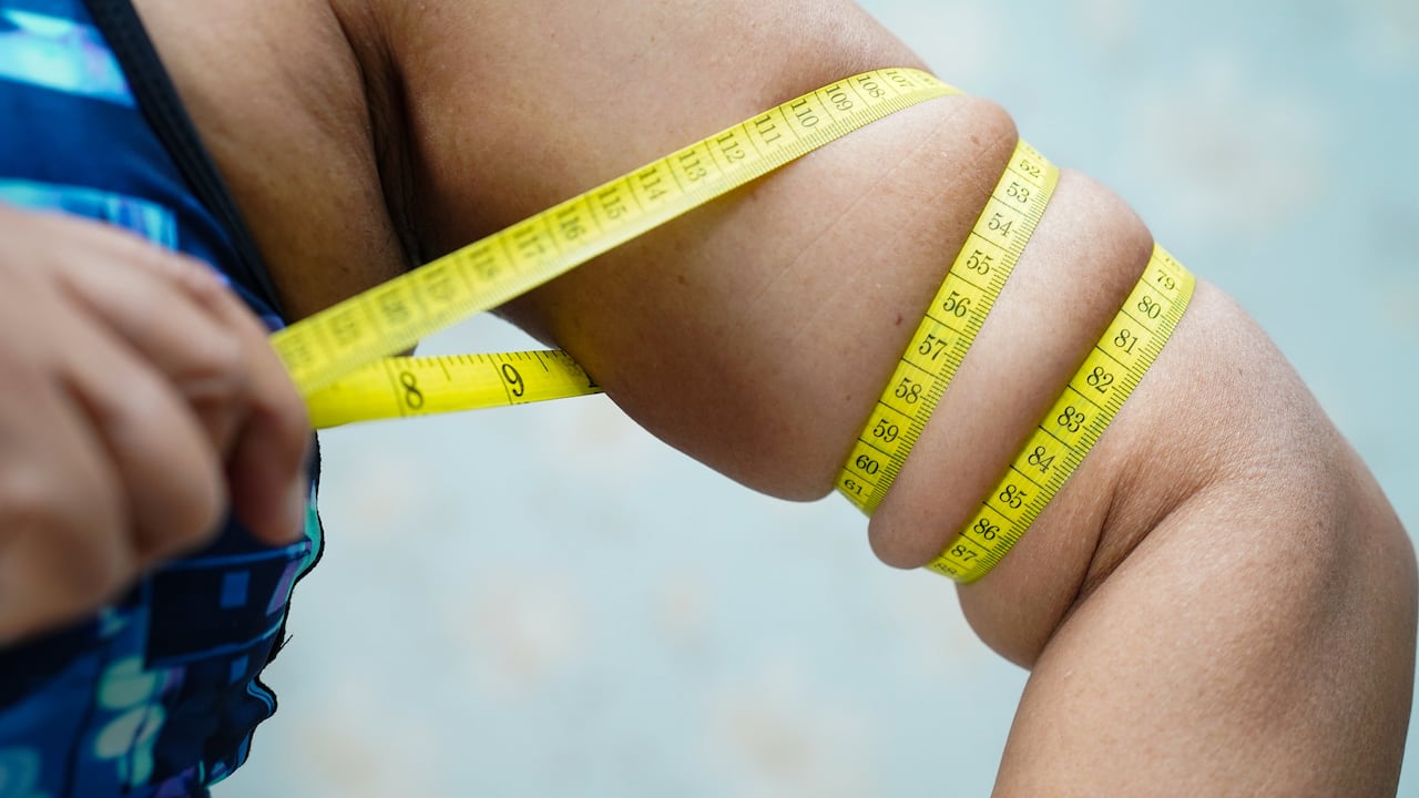 Mujer asiática de mediana edad muestra la grasa corporal del vientre con cinta métrica o cinta de línea con pantalón deportivo.