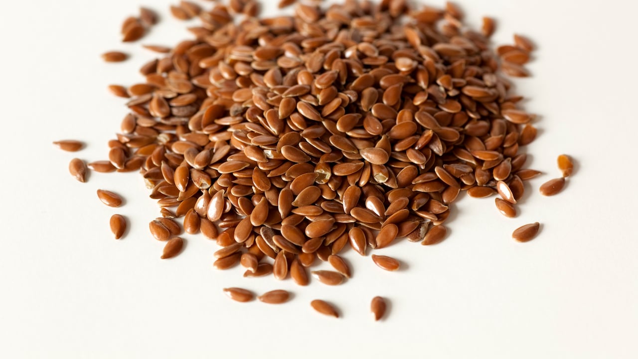 A close up of a pile of dries flax seeds on a white background.