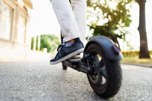 Primer plano de las piernas de un hombre irreconocible montando un scooter eléctrico en la calle de la ciudad.