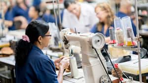 Trabajadora de fabricación femenina que trabaja en una fábrica de calzado usando una máquina de coser industrial